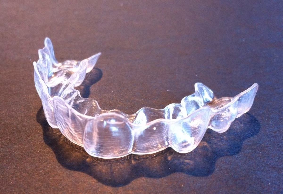 A single clear plastic orthodontic aligner on a dark surface